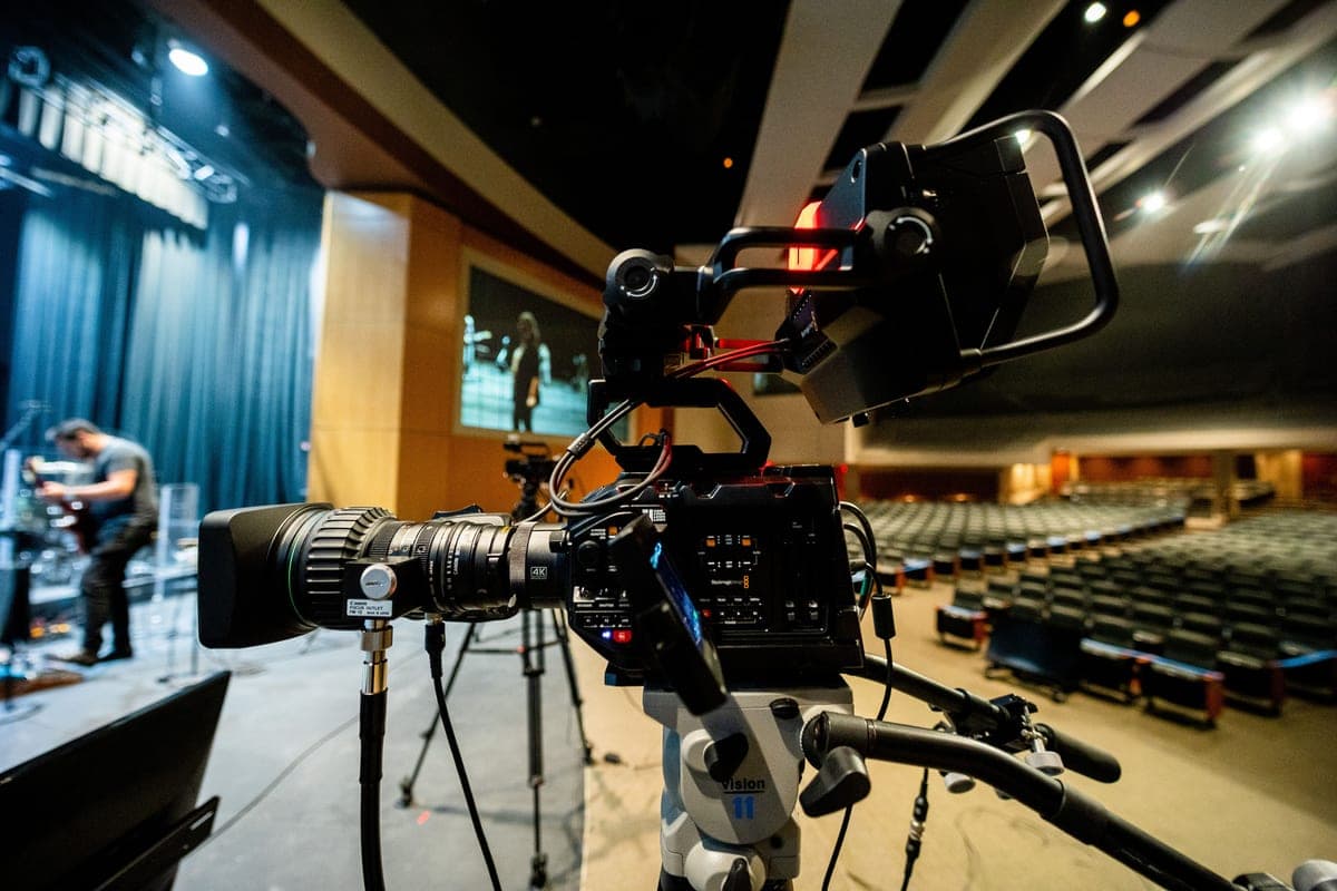 Professional video camera on a tripod beside a stage