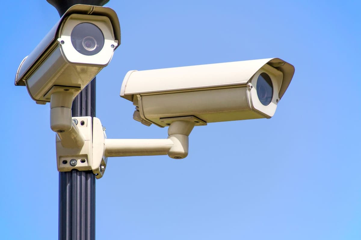 Two outdoor security cameras mounted on a pole against a clear sky